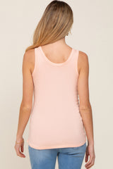 woman wearing a light pink maternity tank top, standing with her back to the camera