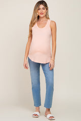 woman wearing a peach maternity tank top and blue jeans, showcasing her baby bump