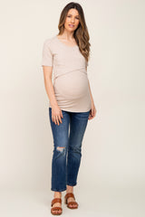 woman wearing a beige short sleeve maternity top over a baby bump with distressed jeans and brown sandals