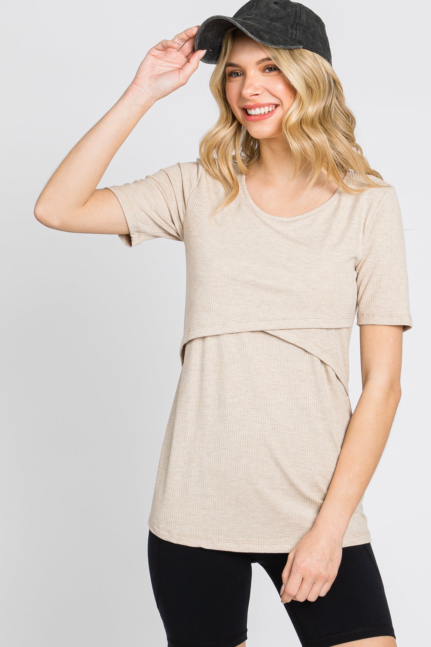 woman wearing a beige short sleeve top with a layered design and smiling while wearing a black cap