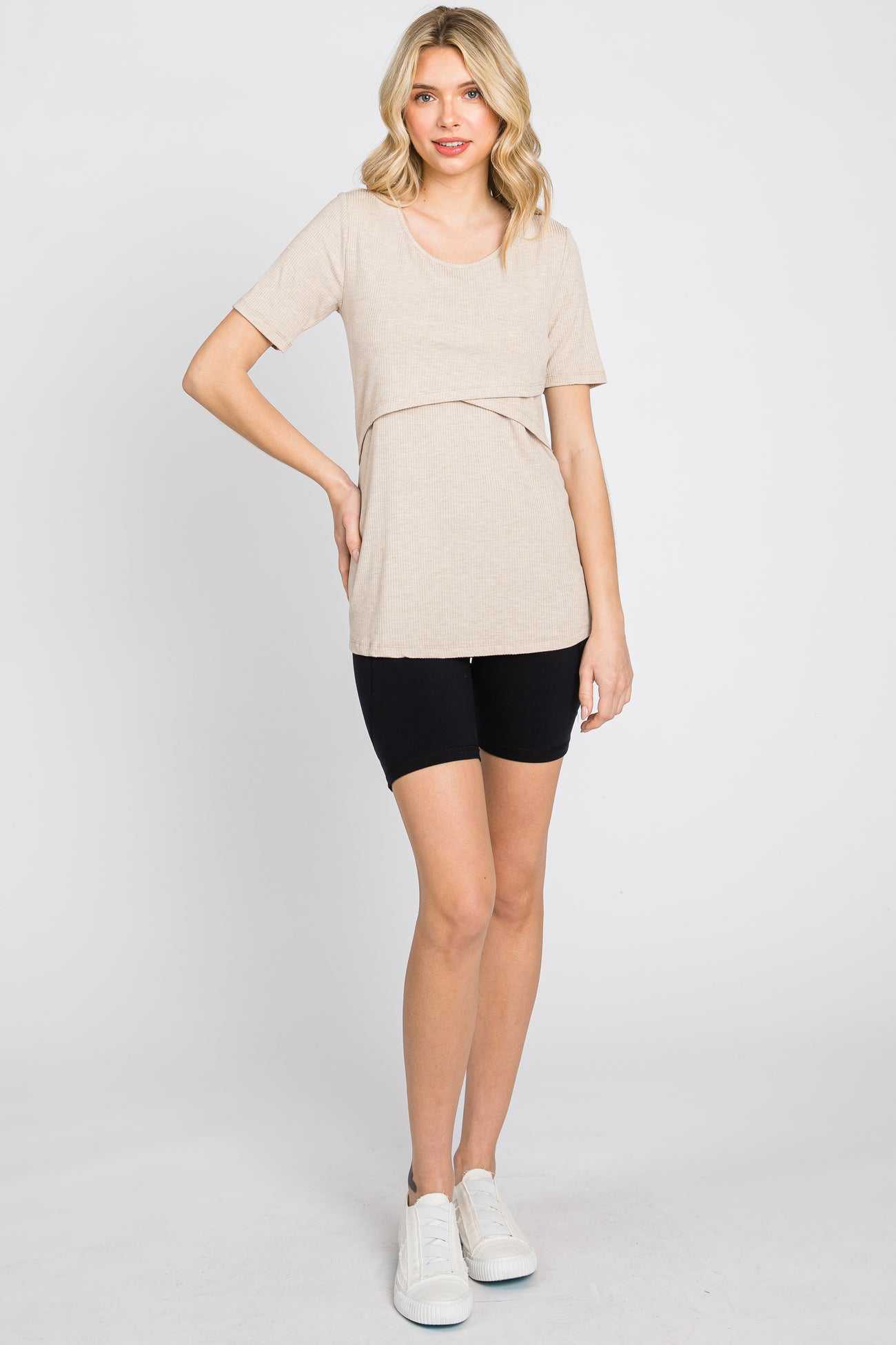 woman wearing a beige short sleeve top with a layered design and black bike shorts, standing on a white background