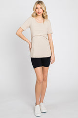 woman wearing a beige short sleeve top with a layered design and black bike shorts, standing on a white background