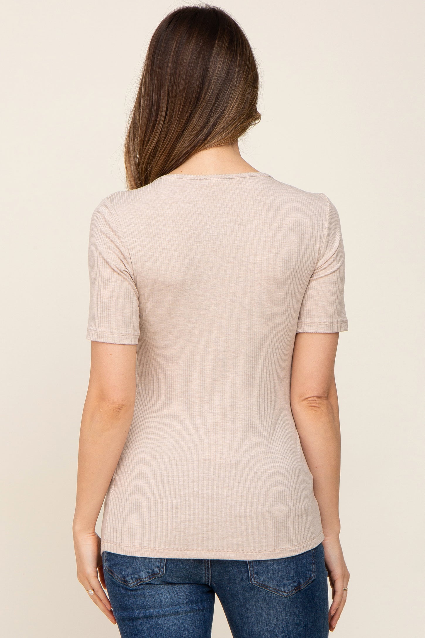 woman wearing a light beige maternity top with short sleeves, viewed from the back, paired with blue jeans