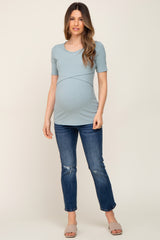 woman wearing a light blue ribbed maternity top and distressed blue jeans, showing her baby bump