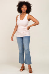 woman wearing a light pink sleeveless top and light blue flared jeans, standing and smiling.
