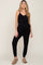 woman wearing a black maternity jumpsuit with a tie waist and tapered leg, posing in a relaxed stance