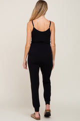 woman wearing a black maternity jumpsuit with fitted legs and adjustable spaghetti straps, showing her back