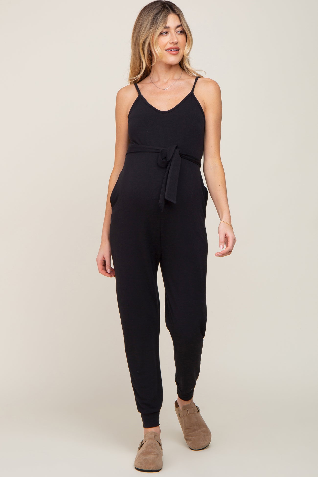woman wearing a black maternity jumpsuit with a tie waist and pockets, showcasing her baby bump