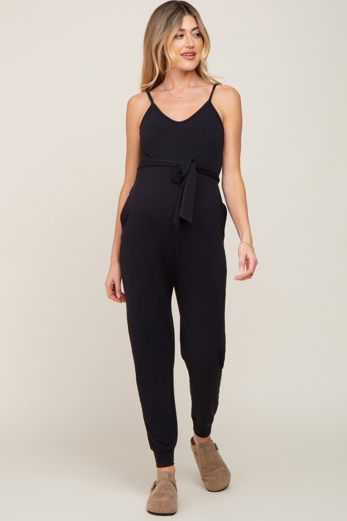 woman wearing a black maternity jumpsuit with a tie waist and pockets, showcasing her baby bump