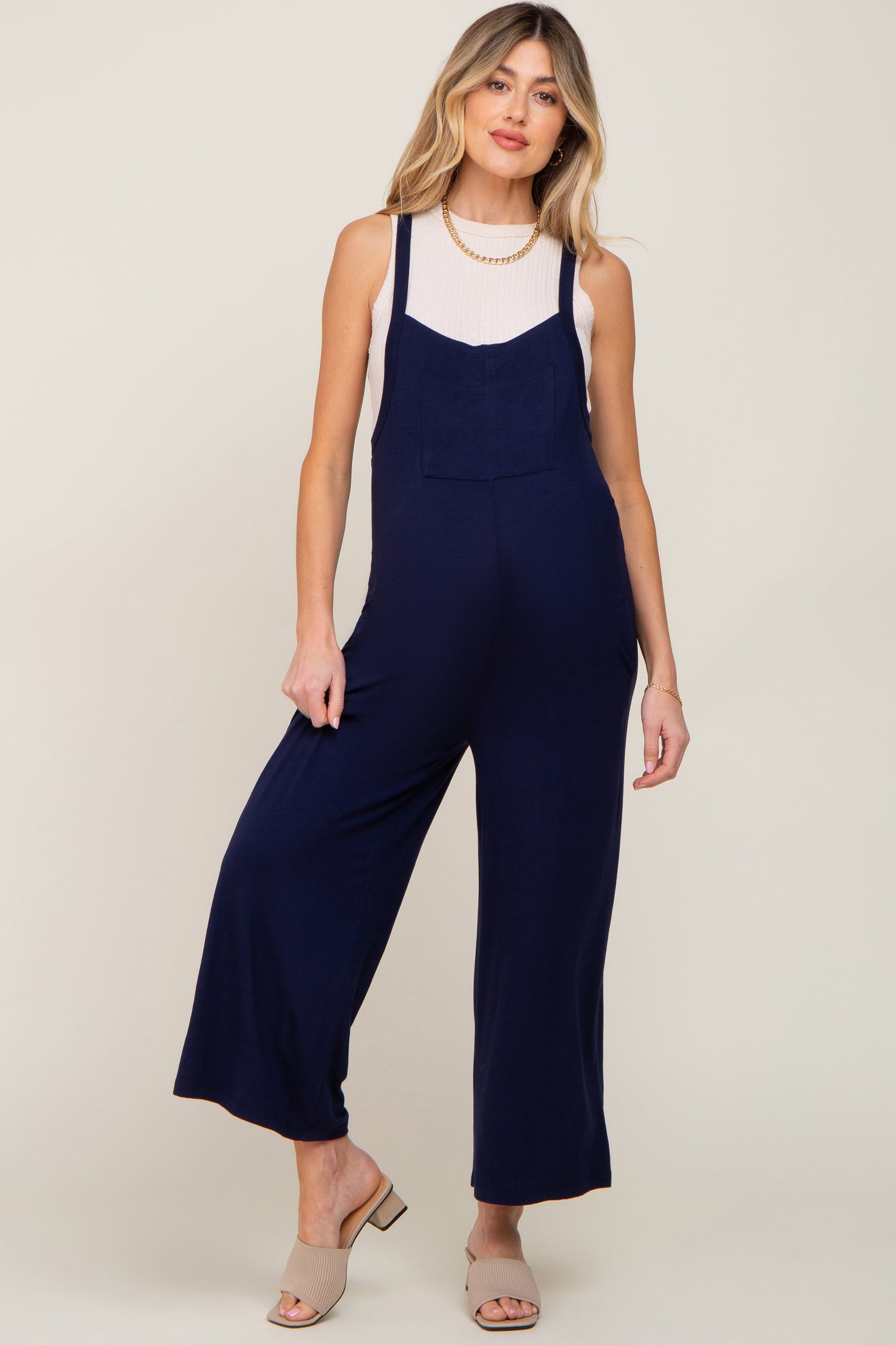 woman wearing a navy blue maternity jumpsuit with wide legs and a pocket, styled with a light top and heels