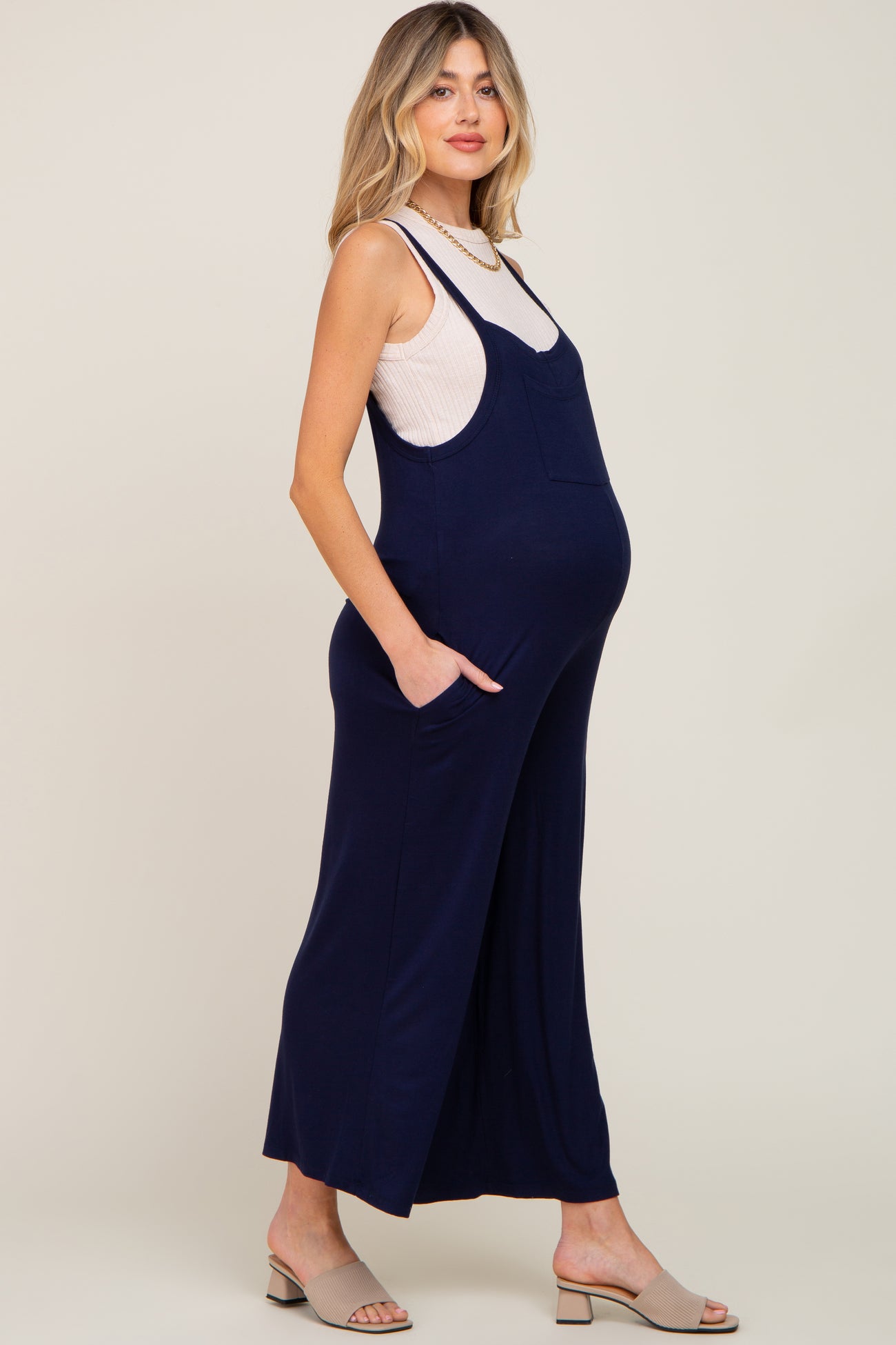 woman wearing a navy blue maternity jumpsuit with pockets and a fitted white tank top, showcasing her baby bump
