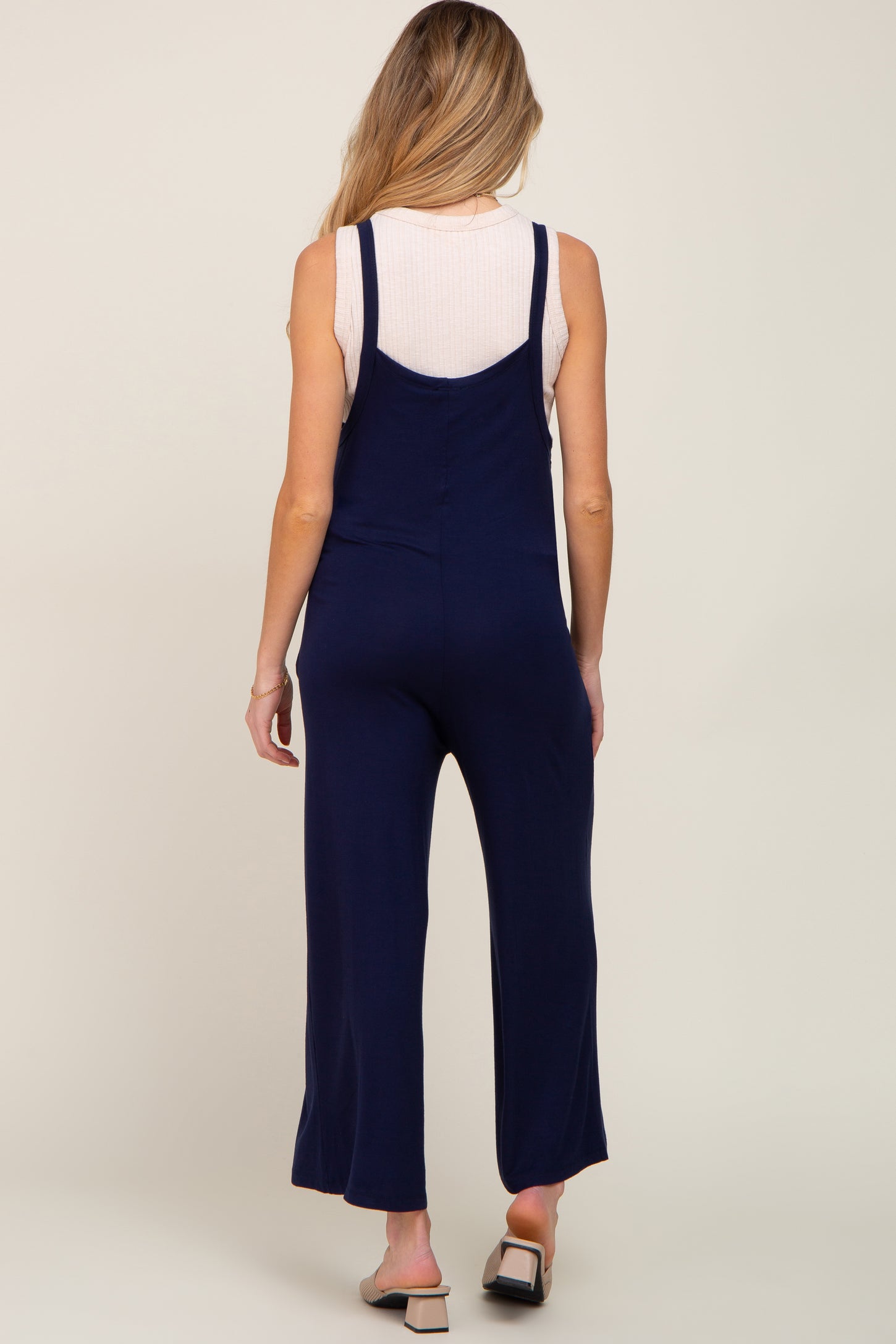 woman wearing a navy blue maternity jumpsuit with adjustable straps, showing the back view.
