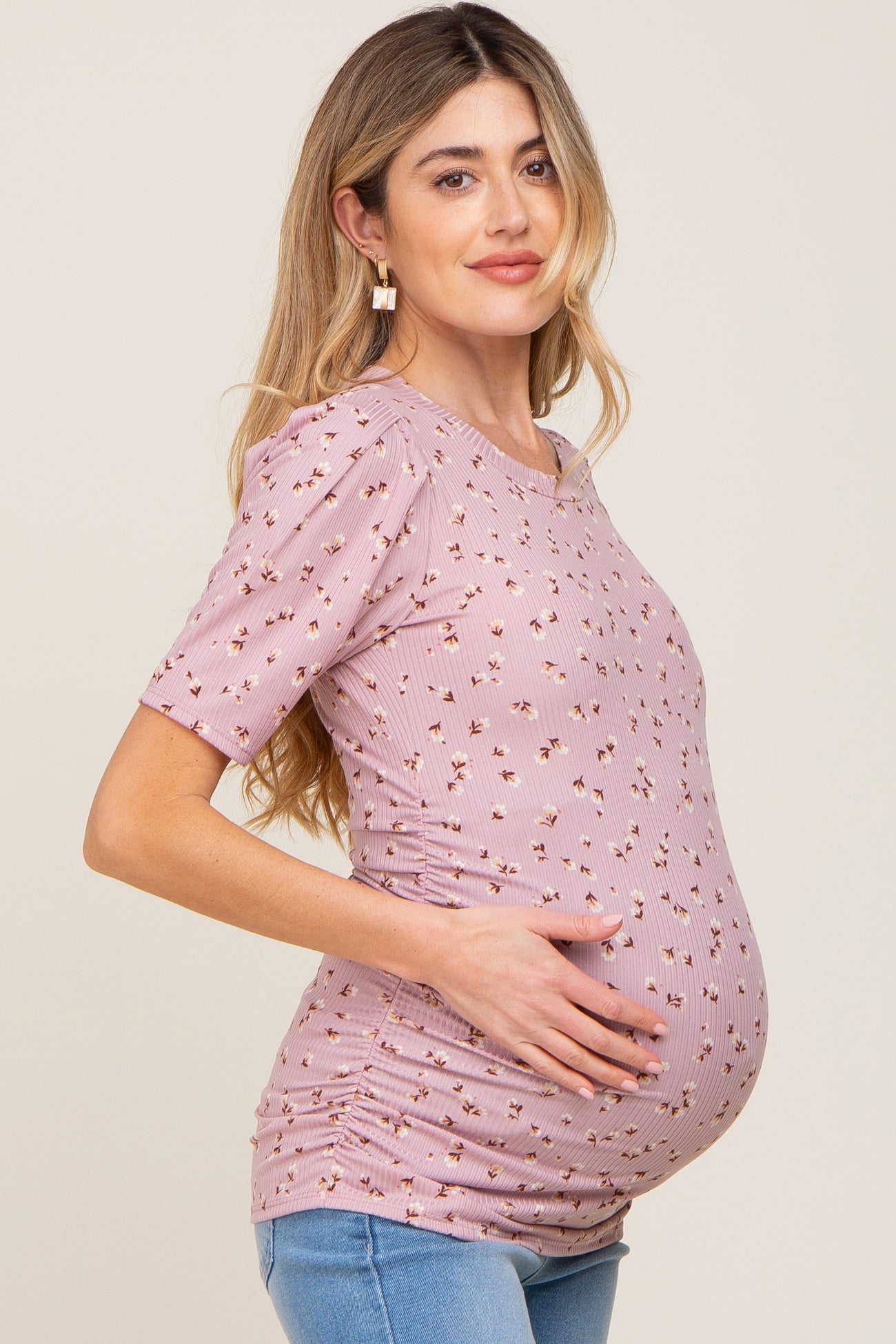 woman wearing a light pink short sleeve maternity top with floral print and holding her baby bump