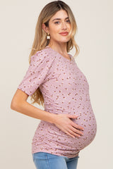 woman wearing a light pink short sleeve maternity top with floral print and holding her baby bump