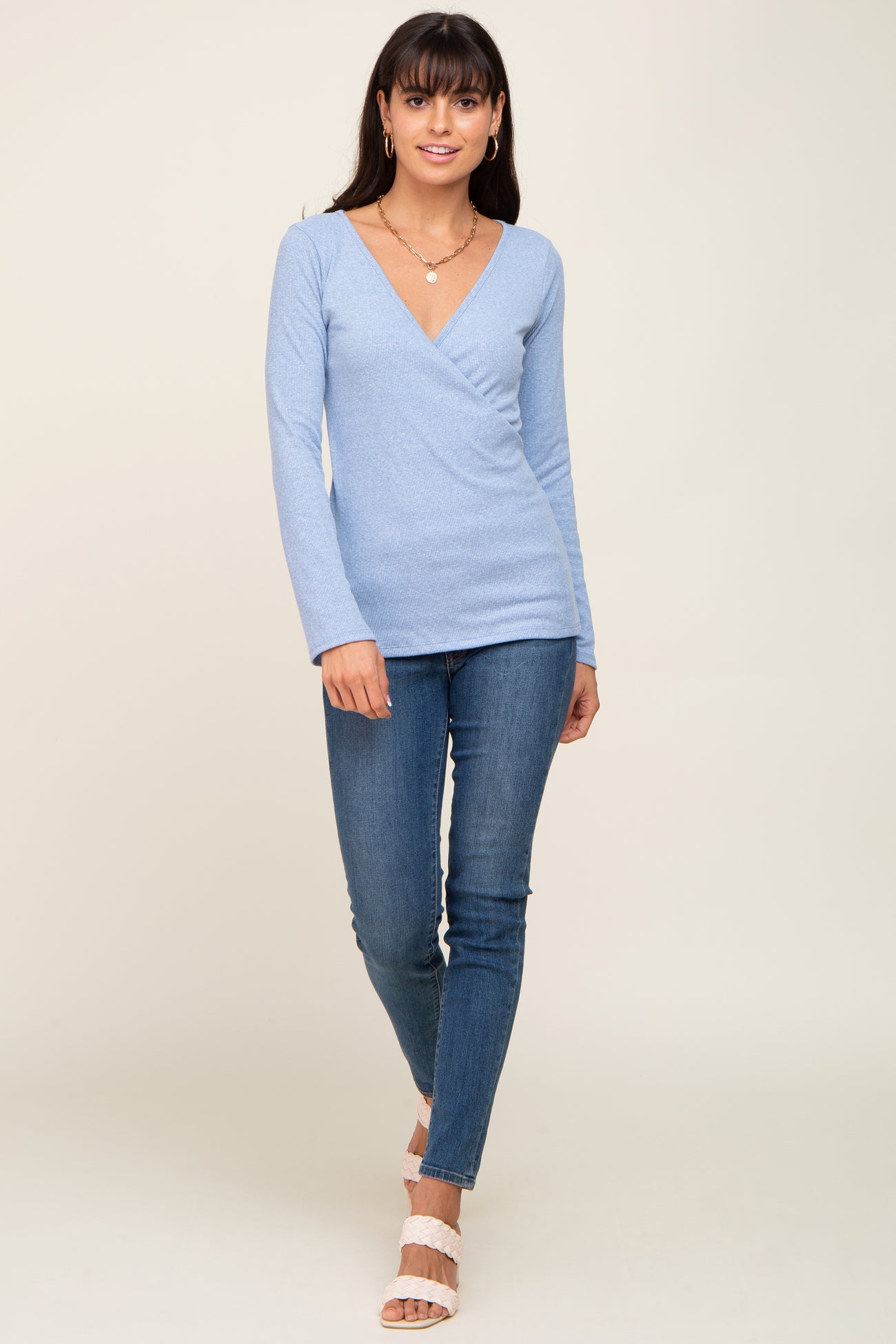 woman wearing a light blue long sleeve wrap top paired with fitted blue jeans and white heeled sandals