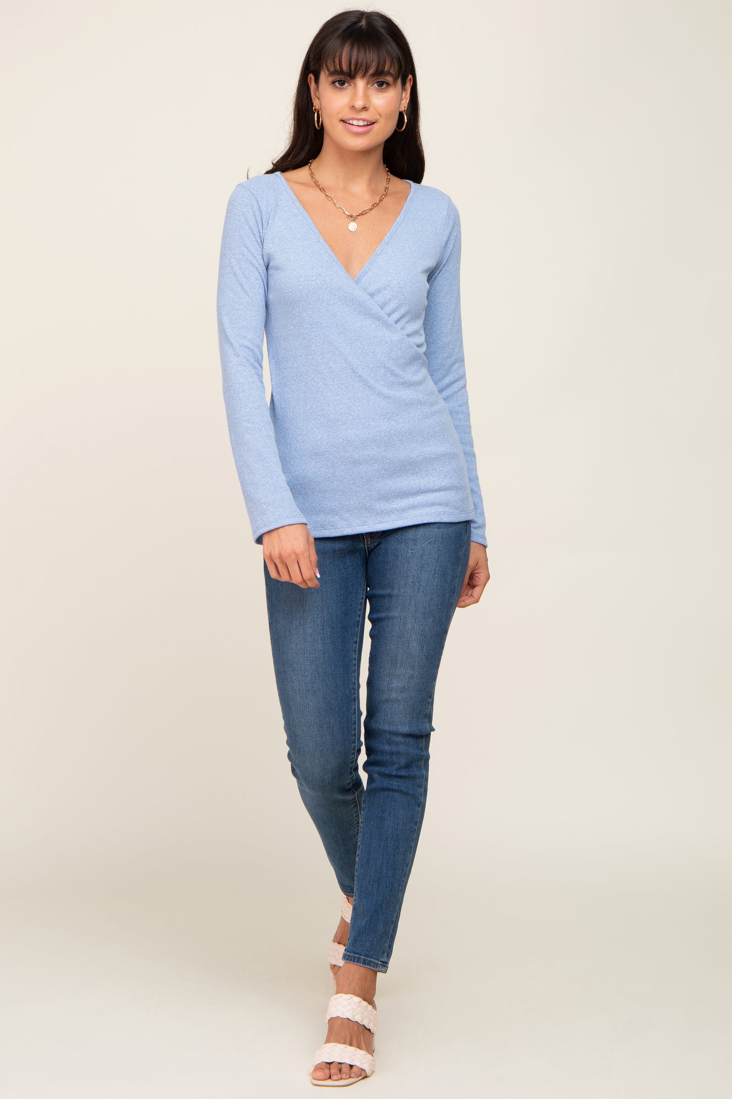 woman wearing a light blue long sleeve wrap top paired with fitted blue jeans and white heeled sandals