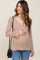 woman wearing a beige long sleeve maternity top with a v-neck and holding her baby bump