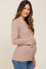 woman wearing a beige long sleeve maternity top, showing her baby bump, paired with blue jeans