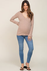 woman wearing a beige long sleeve maternity top with a v-neck and baby bump, paired with blue skinny jeans