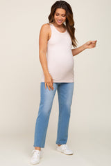 woman wearing a light pink maternity tank top and blue jeans, highlighting her baby bump while smiling.