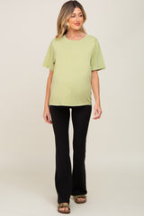 woman wearing a light green maternity t-shirt and black flared pants, showing her baby bump