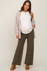 woman wearing a white ribbed maternity tank top, olive wide-leg pants, and a light pink cardigan, showing her baby bump
