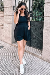 woman wearing a black maternity romper with pockets, styled with sunglasses and white sneakers, walking outdoors