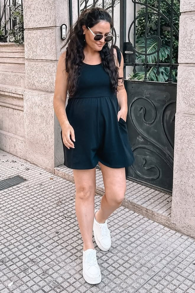 woman wearing a black maternity romper with pockets, walking outside and showcasing her baby bump