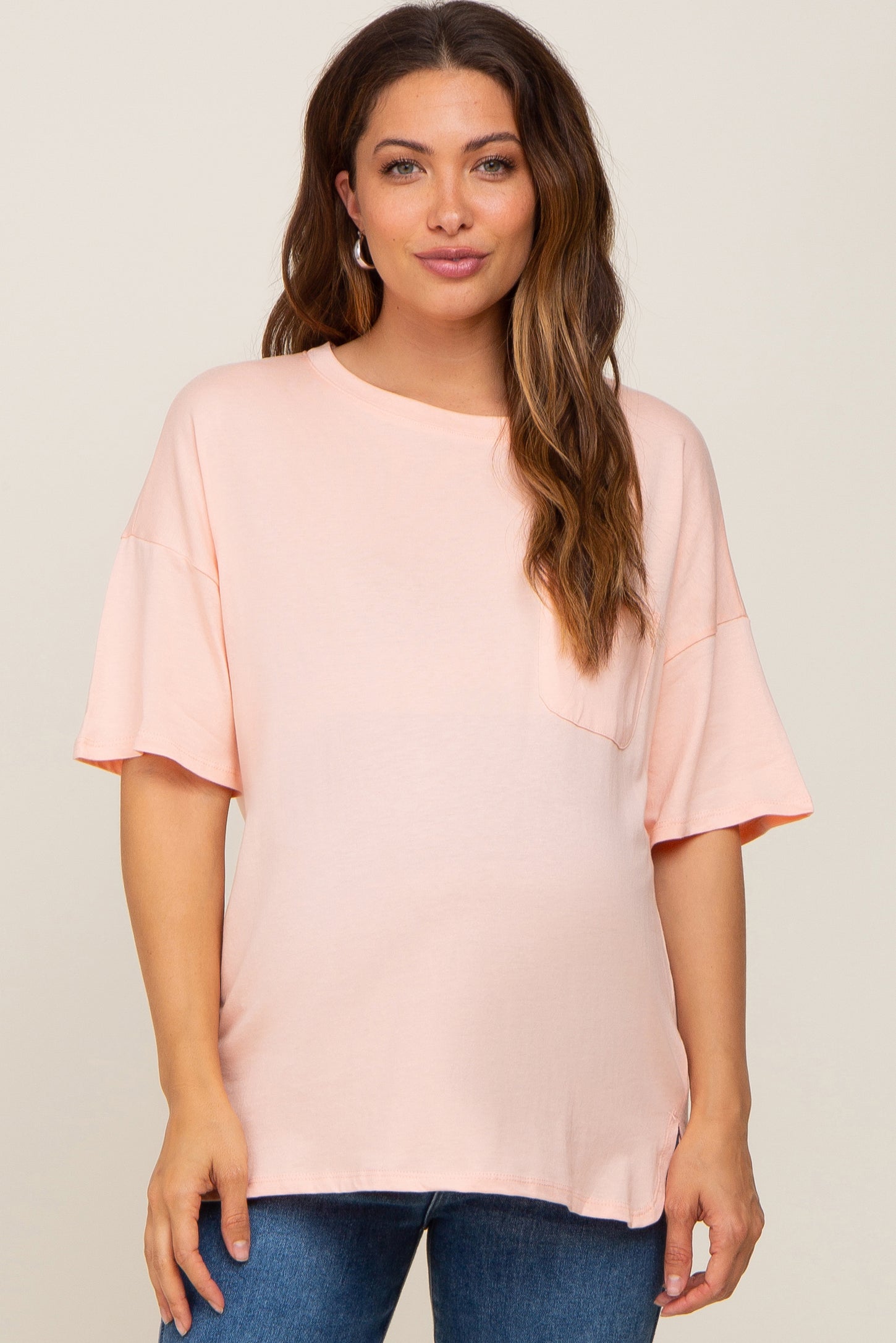 woman wearing a light peach oversized maternity t-shirt with short sleeves and a pocket on the front