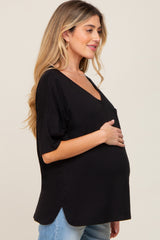 Pregnant woman wearing a black v-neck maternity top and jeans while holding her baby bump