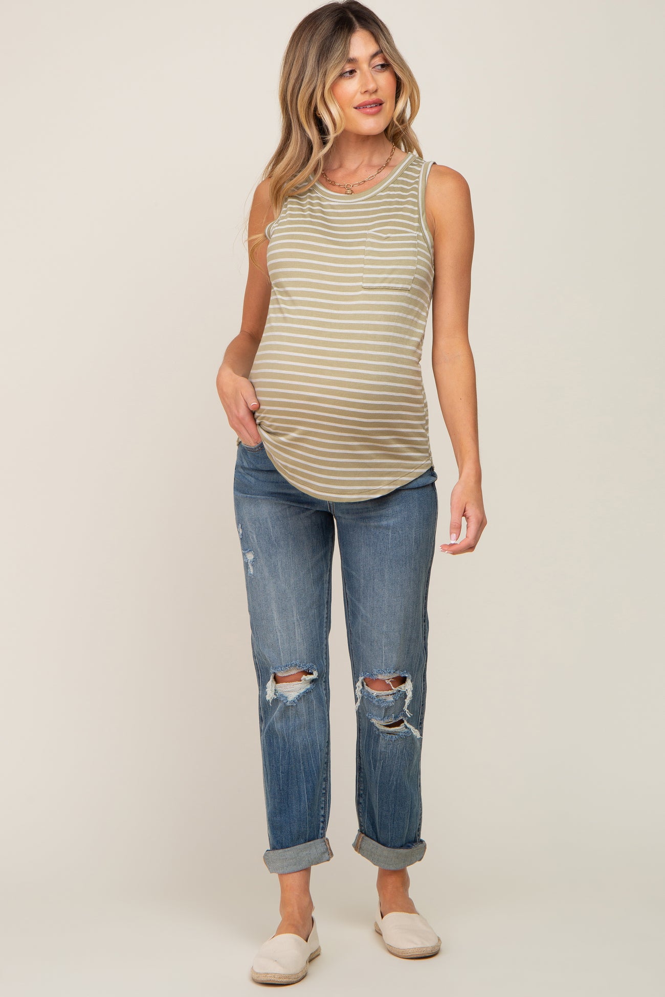 woman wearing a striped olive green maternity tank top and distressed blue jeans, showing her baby bump