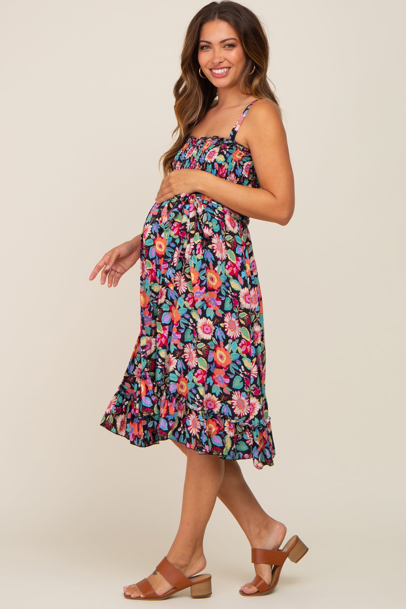 woman wearing a colorful floral maternity dress with adjustable straps and a ruffled hem, showing her baby bump