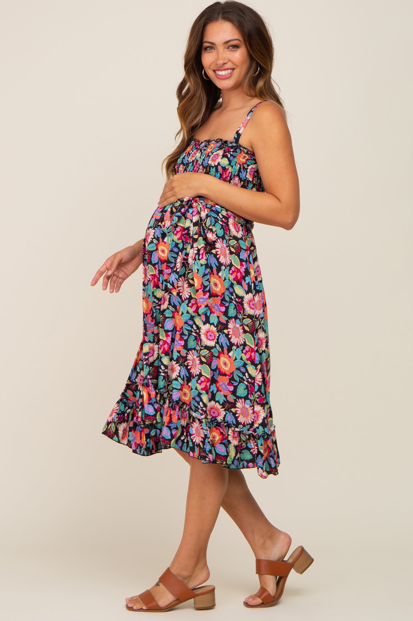 woman wearing a colorful floral maternity dress with adjustable straps and a ruffled hem, showing her baby bump
