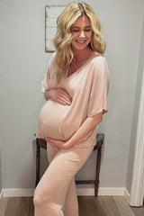 woman wearing a blush pink maternity loungewear set, smiling and holding her baby bump