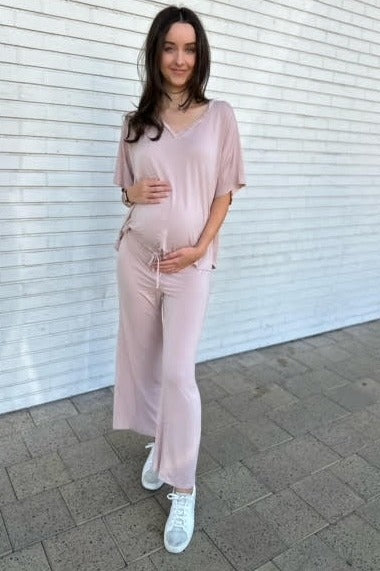 woman wearing a light pink maternity set with a relaxed fit and holding her baby bump