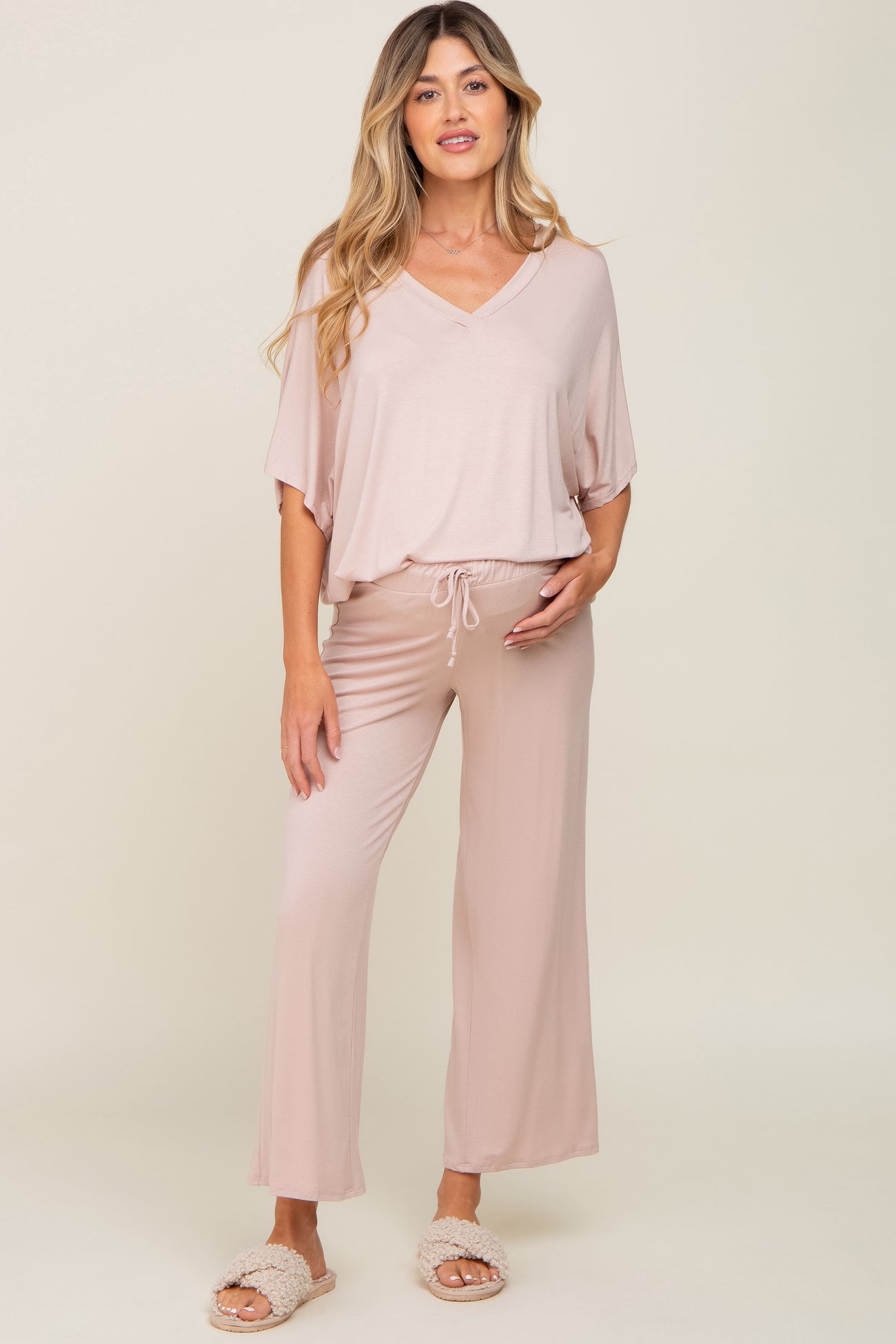 woman wearing a light pink maternity lounge set with a v-neck top and wide-leg pants, holding her baby bump
