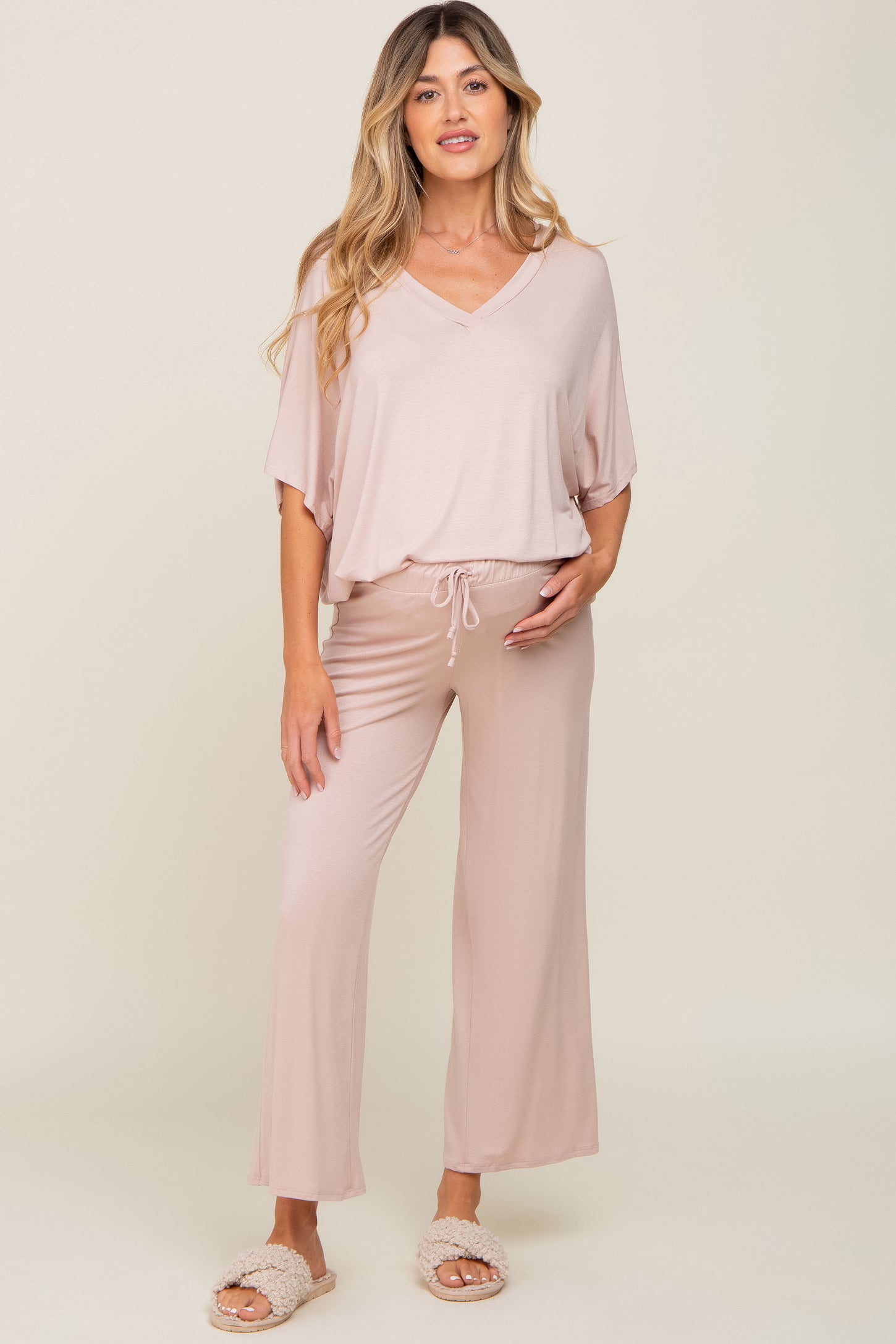 woman wearing a light pink maternity lounge set with a v-neck top and wide-leg pants, holding her baby bump