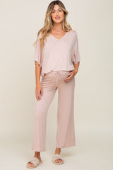woman wearing a light pink maternity lounge set with a v-neck top and wide-leg pants, holding her baby bump