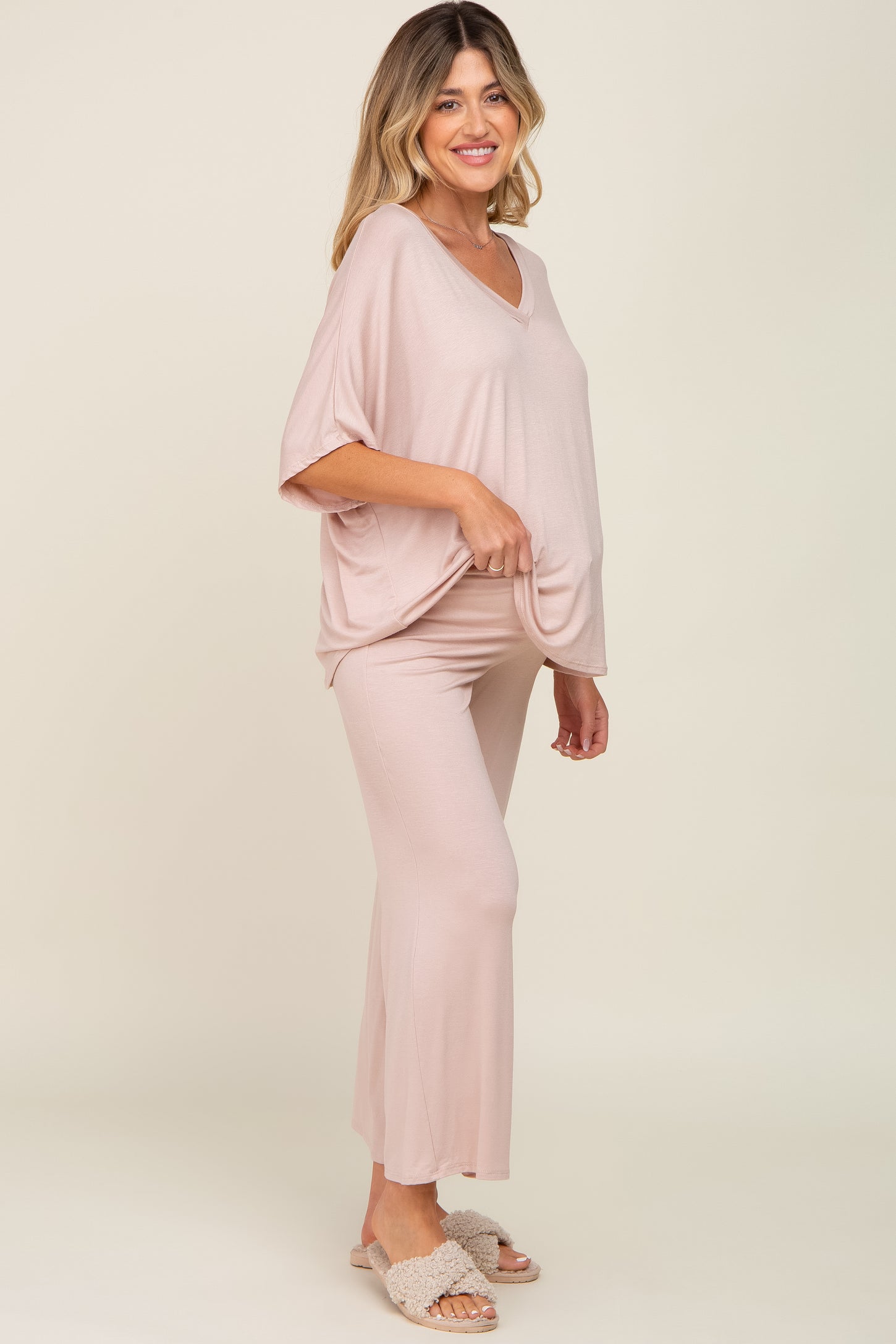 woman wearing a light pink maternity lounge set with a loose top and flared pants, styled with fuzzy slippers