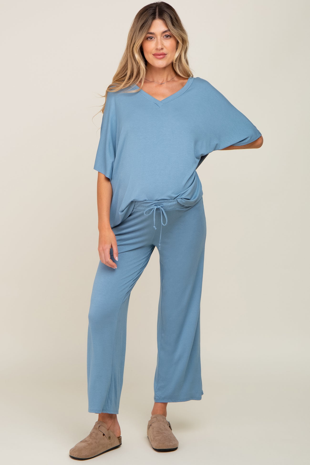 woman wearing a blue maternity jumpsuit with a v-neck and drawstring waist, standing with relaxed fit pants