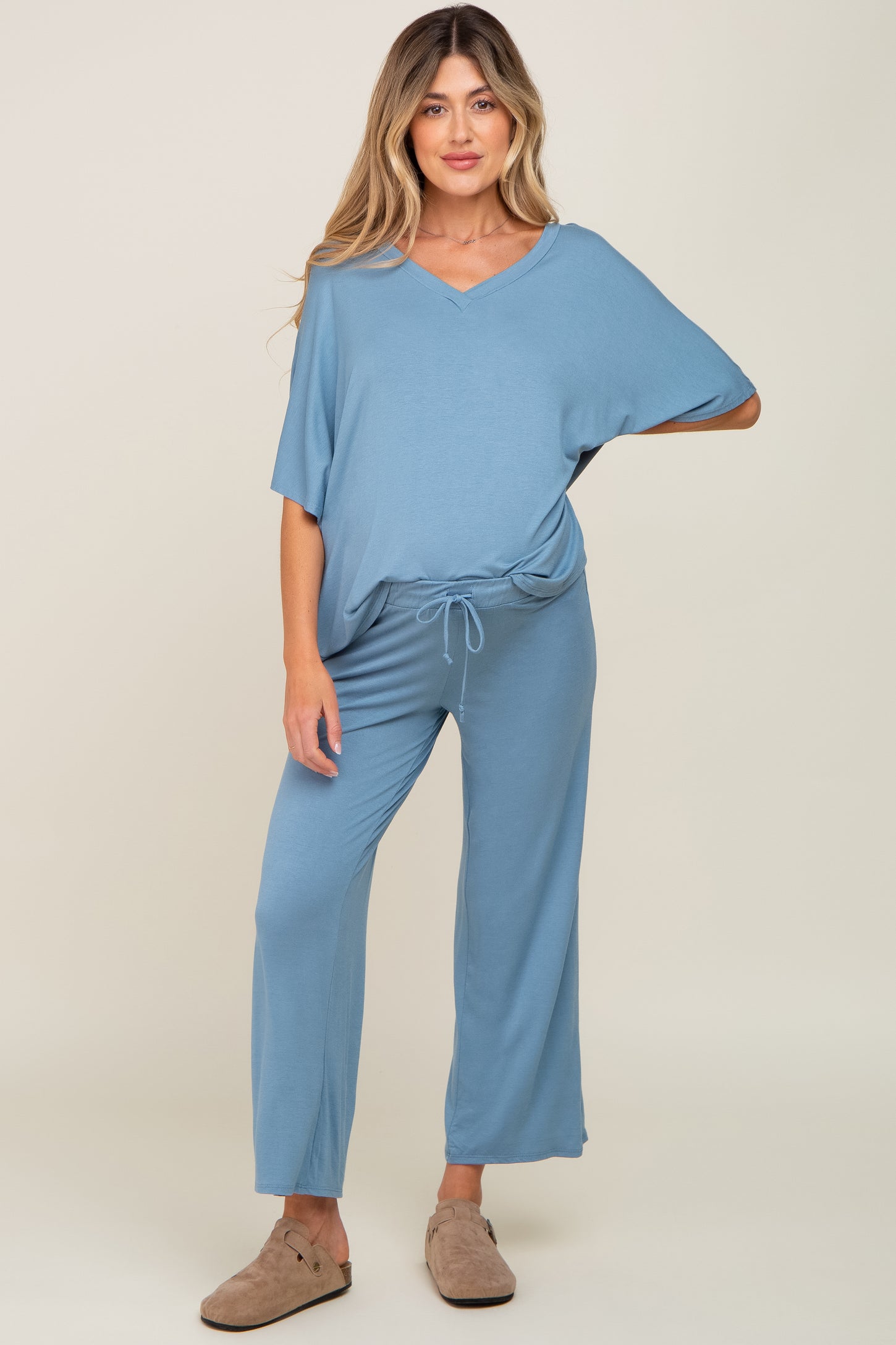 woman wearing a blue maternity jumpsuit with a v-neck and drawstring waist, standing with relaxed fit pants