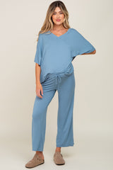 woman wearing a blue maternity jumpsuit with a v-neck and drawstring waist, standing with relaxed fit pants