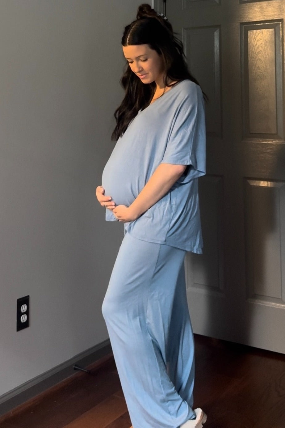 woman wearing a light blue maternity loungewear set, showing her baby bump while standing sideways