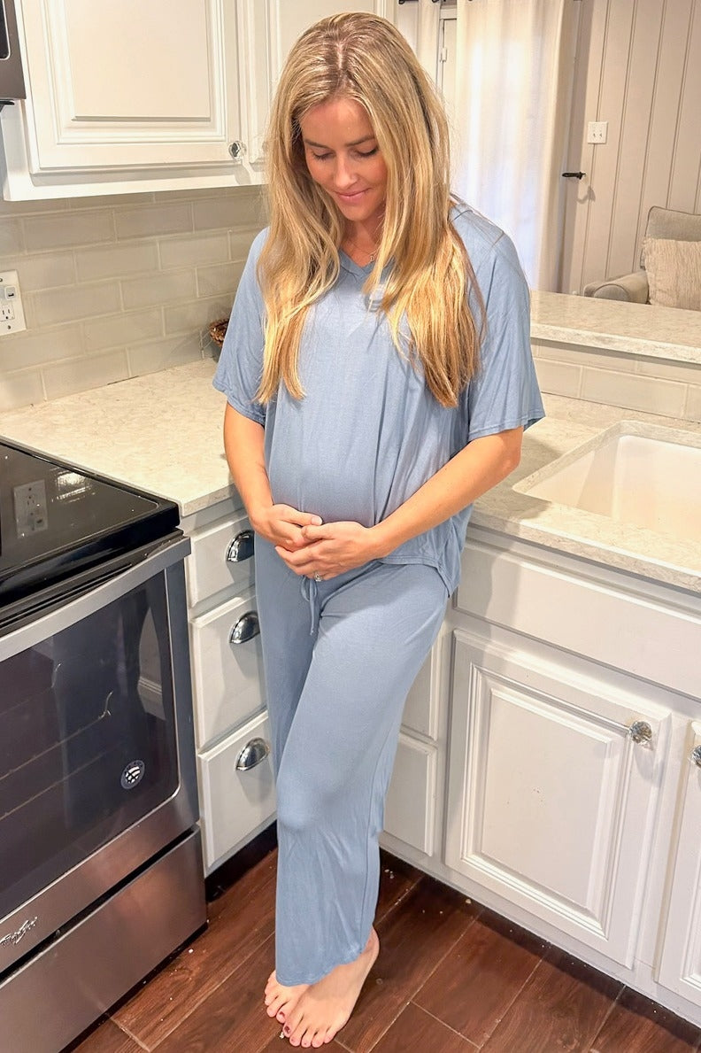 woman wearing a light blue maternity loungewear set with a loose top and wide-leg pants, gently cradling her baby bump