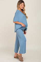 woman wearing a light blue maternity top and matching pants, showing her baby bump and styled with casual footwear