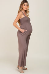 woman wearing a brown maternity jumpsuit with smocked bodice and side pockets, showing her baby bump