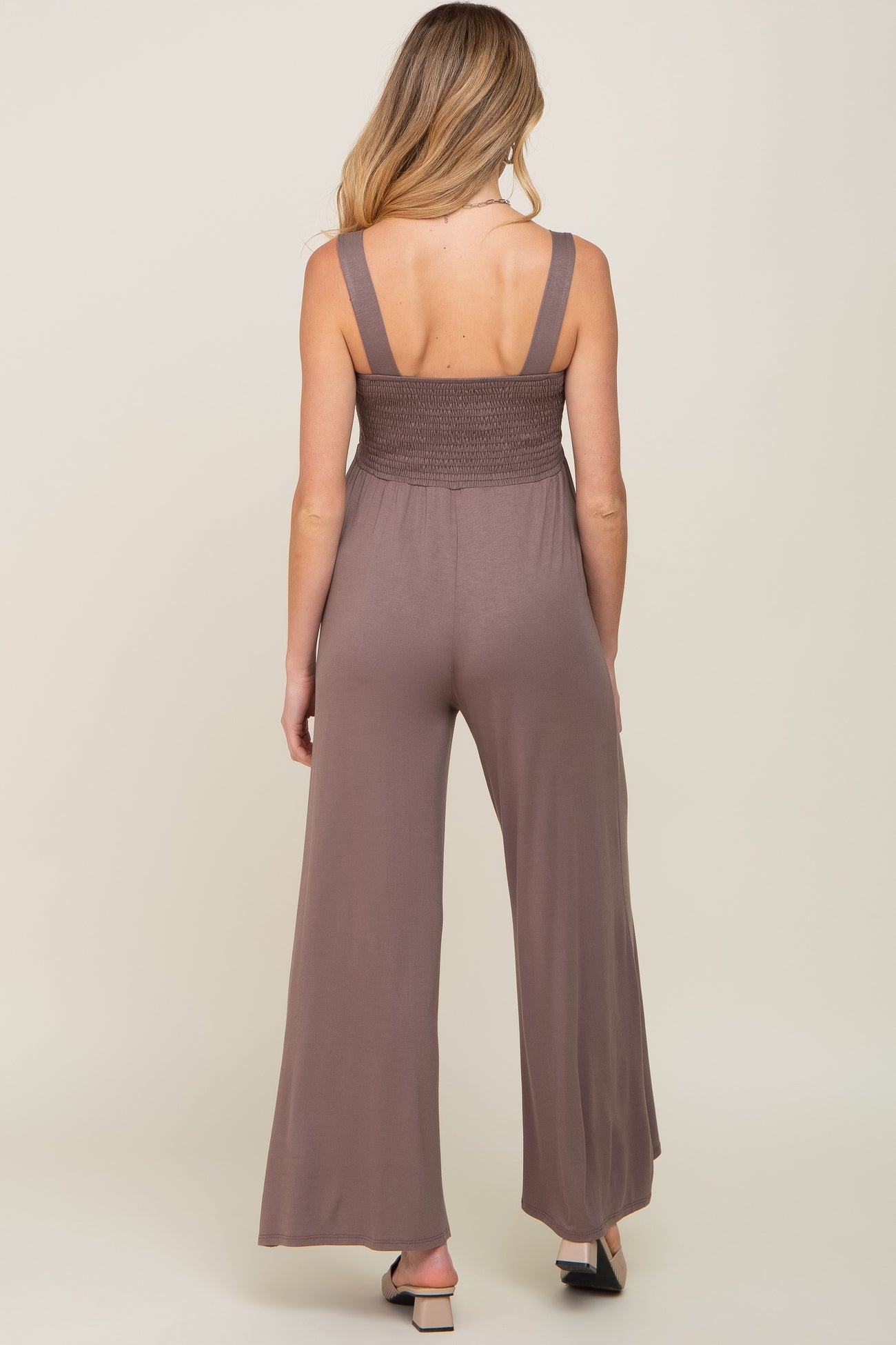 woman wearing a brown maternity jumpsuit with a smocked bodice and wide leg bottoms, view from the back
