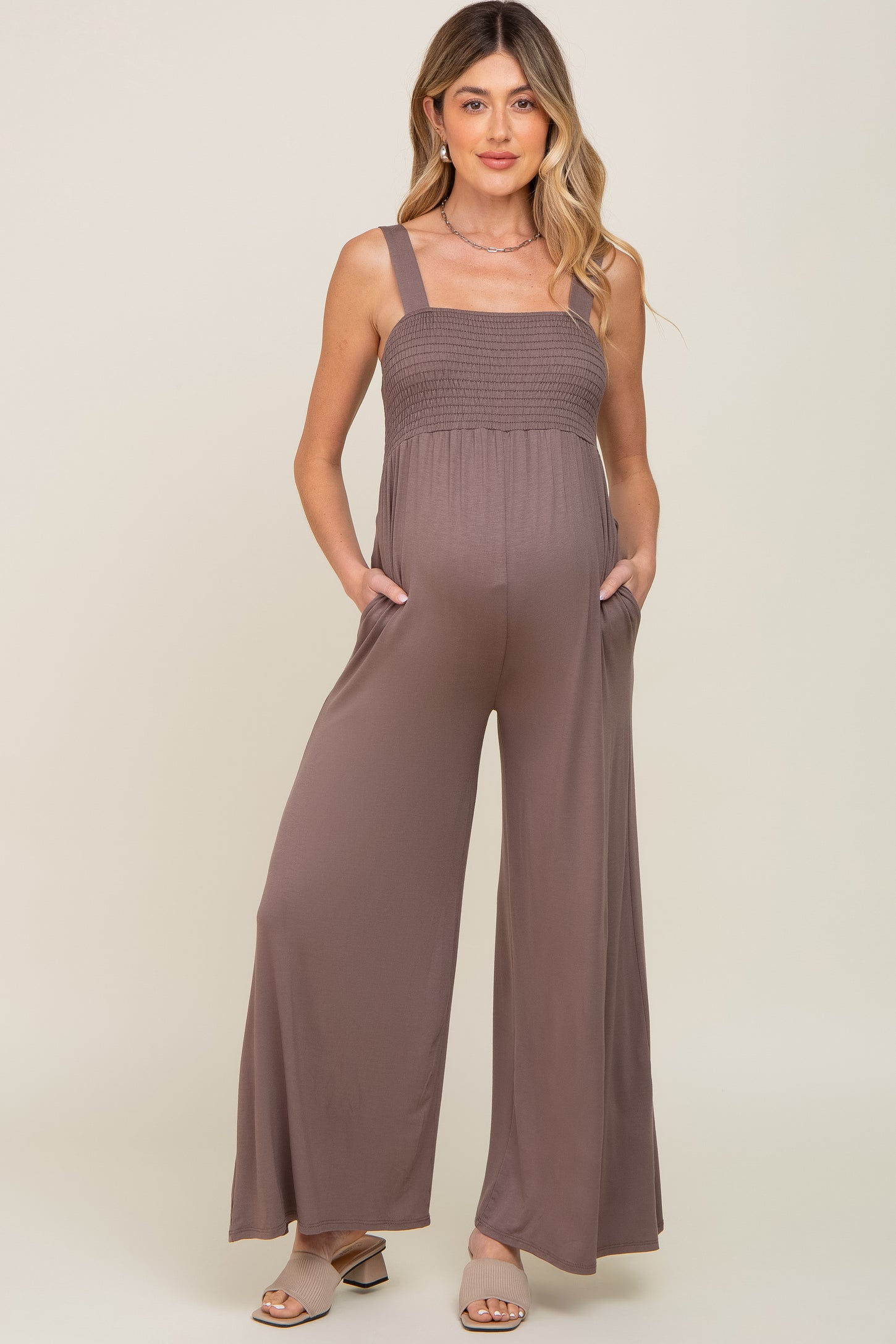 woman wearing a dusty mauve maternity jumpsuit with smocked bodice and pockets, showcasing her baby bump