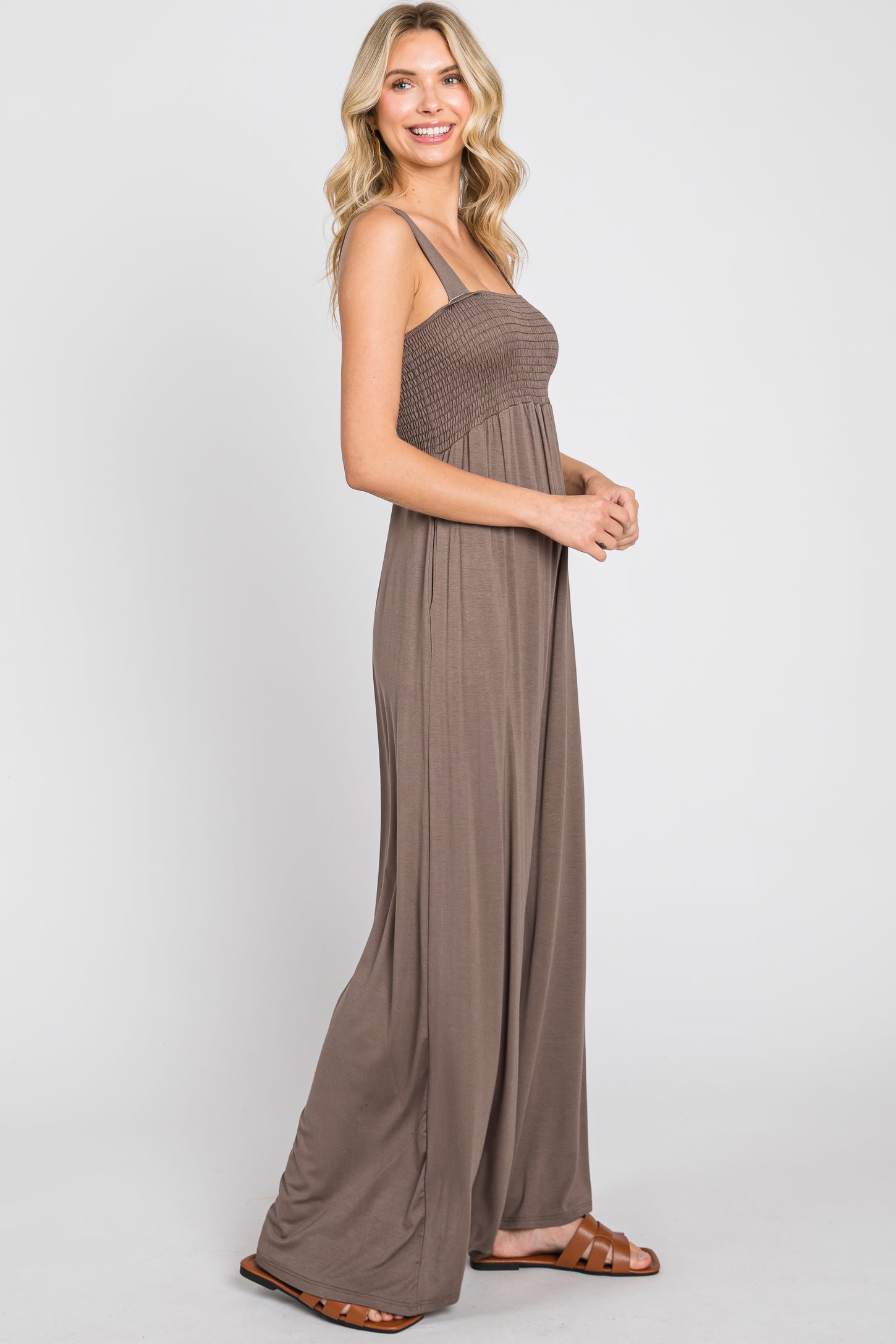 woman wearing a brown smocked bodice maxi dress with thin straps standing sideways