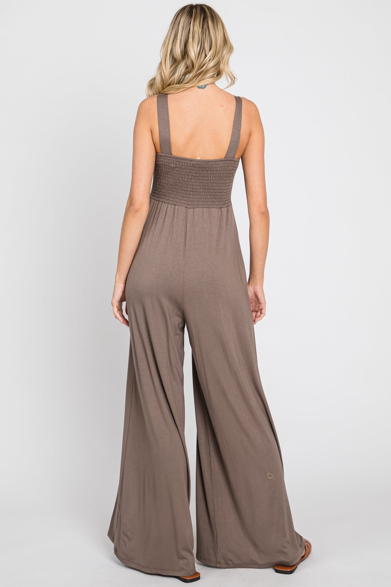 woman wearing a brown sleeveless backless jumpsuit with wide leg pants and a smocked bodice